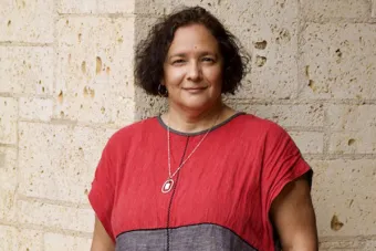A woman in a red shirt stands in front of a brick wall