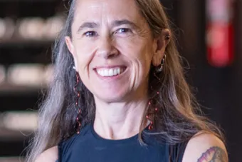 A person with long gray hair and tattoos smiles