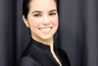 An image of ballerina Veronica Boccardo, wearing a black turtle neck with brunette hair that is wrapped in a bun 