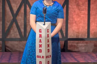 Lilly Lane Stafford stands on a stage at a microphone dressed as Patsy Cline.