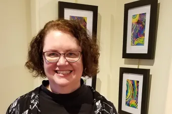 Marcia standing in front of three pieces of art hanging on a wall