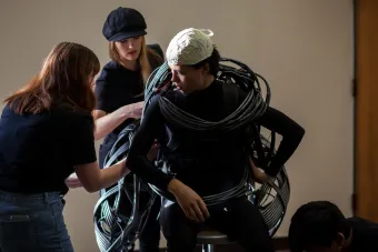 Students help dress an actor in a raptor costume