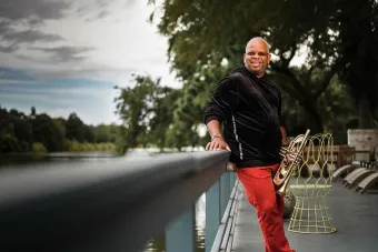 Terence Blanchard leaning on a bridge outside holding his trumpet.