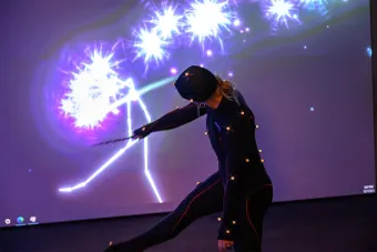 A dancer wearing motion sensors waves a wand to manipulate projection on a screen