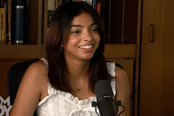 Ahana Bhat talking into a mic with a bookcase in the background