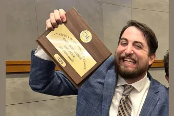 Alum and theatre educator Cody Edgar smiles and holds up an Advancing State One-Act Play plaque