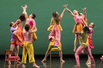 Dancers from the Mark Morris Dance perform on stage with folding chairs and brightly colored costumes