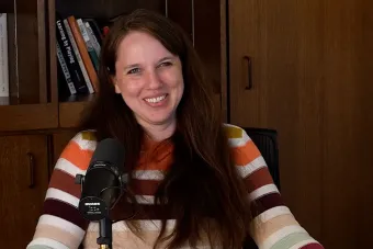 Adrienne Pedrotti Bingamon sitting in front of a bookshelf talking into a mic