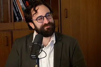 Michael Smith Talking into a mic with a bookshelf in the background