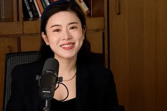 Jinni Shen talking into a mic with a bookshelf in the background