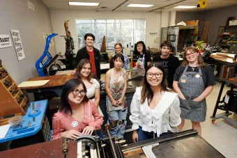 Students stand around posters printed in the Print Lab in the Department of Design