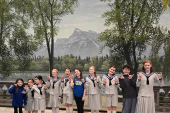 The cast of the touring production of The Sound of Music poses in front of the backdrop used in the film in Texas Performing Arts scenic shop.