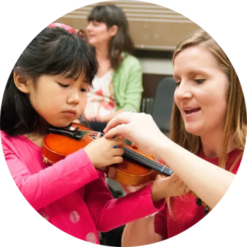A UTeach Music student works with a young student on violin.