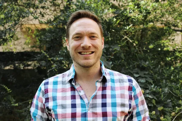 Headshot of oboist Andrew Parker standing outside in front of trees wearing a checkered shirt.