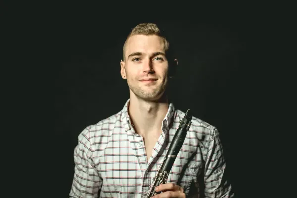 A headshot of clarinetist Tyler Webster wearing a checkered shirt holding his instrument.