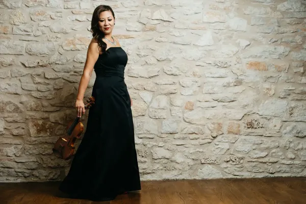 Violinist Sandy Yamamoto holds her violin wearing a black strapless gown.
