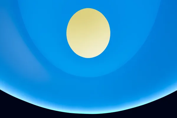 A blue lit curved interior features a circular oculus at the top that opens to a yellow sky.