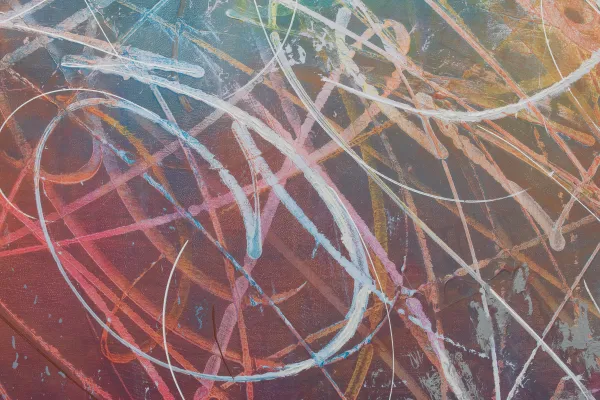 A close up of an abstract painting, featuring white scribbles across a rainbow gradient background.