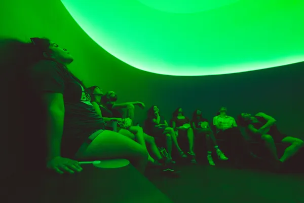 Visitors sit in a green lit curved room looking up.