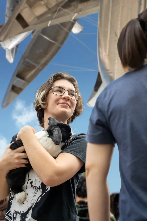Outside, a student holds a bunny in their arms. Above the student is a sculpture made of silver canoes.