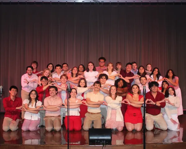 Members of the Longhorn Singers makes heart shapes with their hands and smile for the camera on stage.
