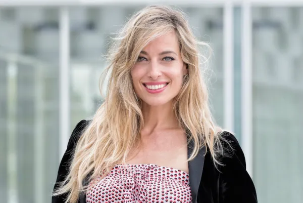 Blonde women smiling in front of camera-blurred back drop.