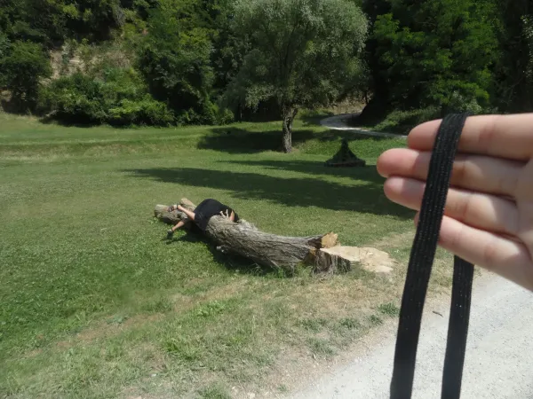 scene with person draped over downed tree trunk with hand in foreground holding black strap