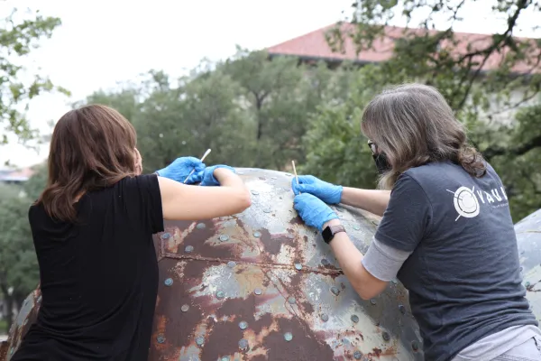 Two volunteers add new pennies to an artwork