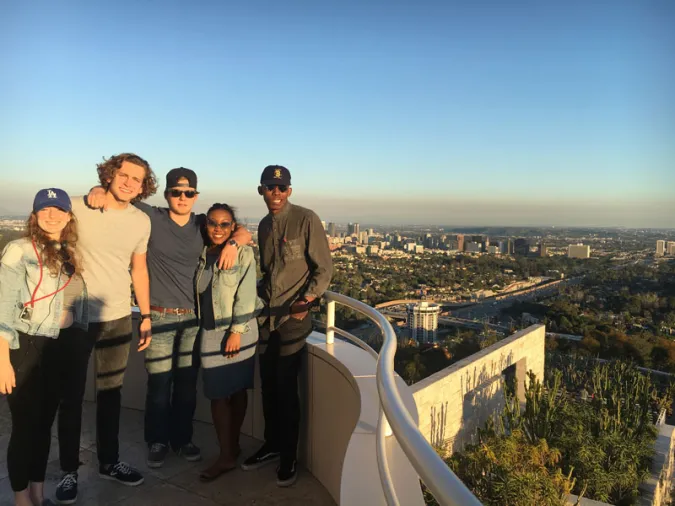Five students pose on a balcony of the Getty Center with the Los Angeles skyline in the background