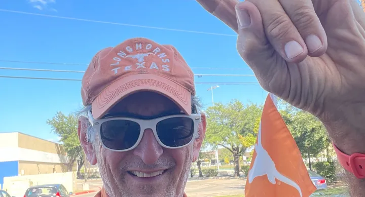 Holt Pierce wearing Longhorn hat and shirt, raising his hand in a hook 'em position