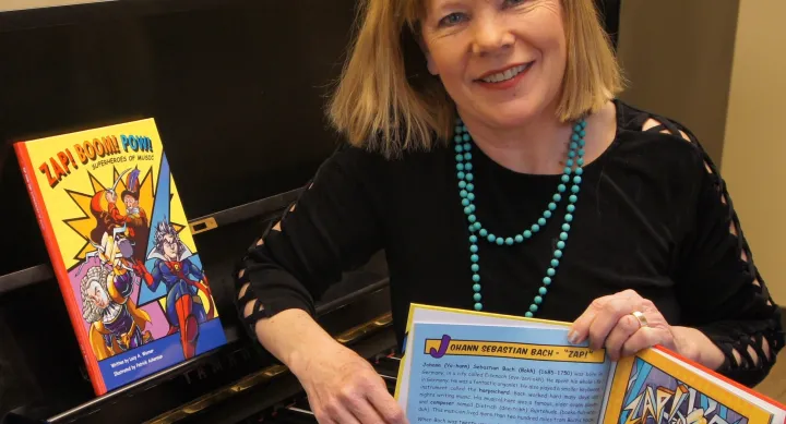 Lucy Amen Warner holds a copy of her children's book while sitting at a piano