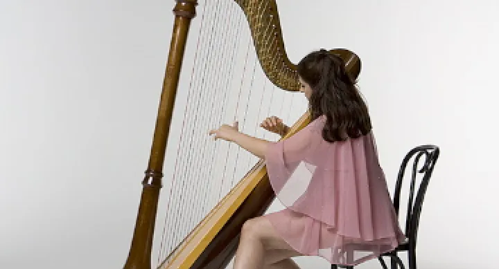 Mia Theodoratus wears a pink dress and plays the harp