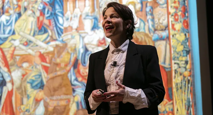 A speaker stands in front of a colorful background while addressing an audience