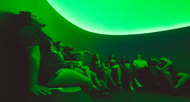 Visitors sit in a green lit curved room looking up.