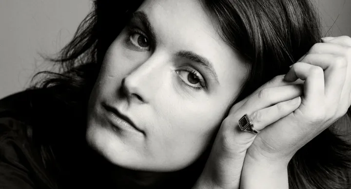 A black and white portrait of a woman from the neck up. Her head is resting on her two hands that are clasped to the side of her face.