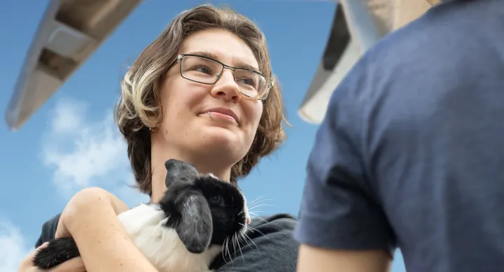 Outside, a student holds a bunny in their arms. Above the student is a sculpture made of silver canoes.