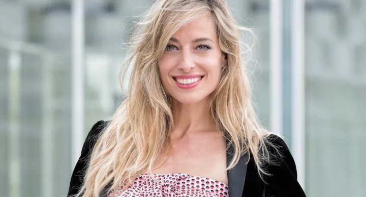 Blonde women smiling in front of camera-blurred back drop.