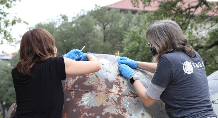 Two volunteers add new pennies to an artwork