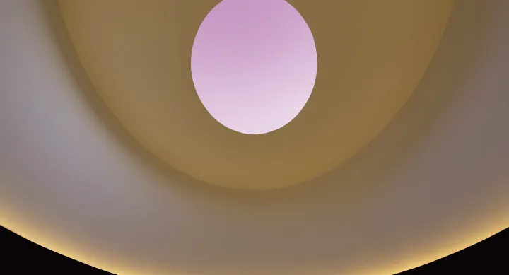 Ceiling of james turrells skyspace, featuring an orange lit wall and an occulus with a pink sky