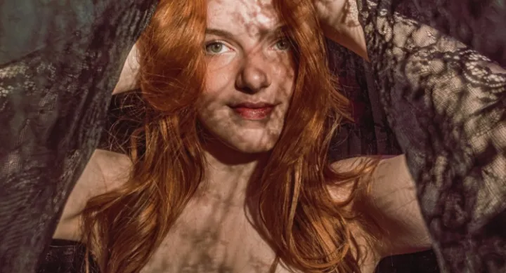 A headshot of a red haired woman under a black lace cloth