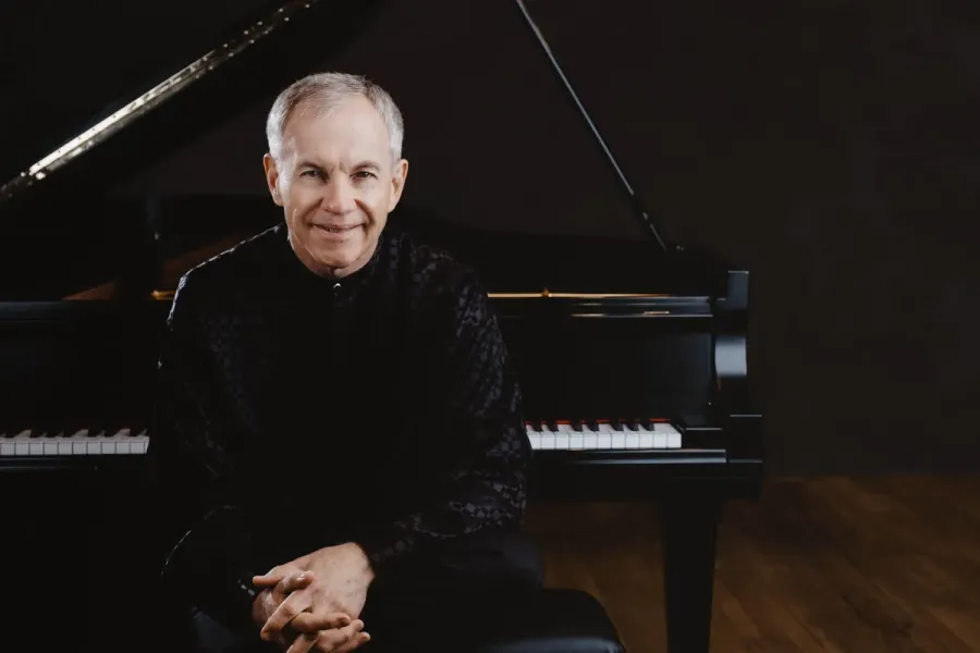 Pianist Anton Nel sits on a bench in front of an open 9-foot grand piano.
