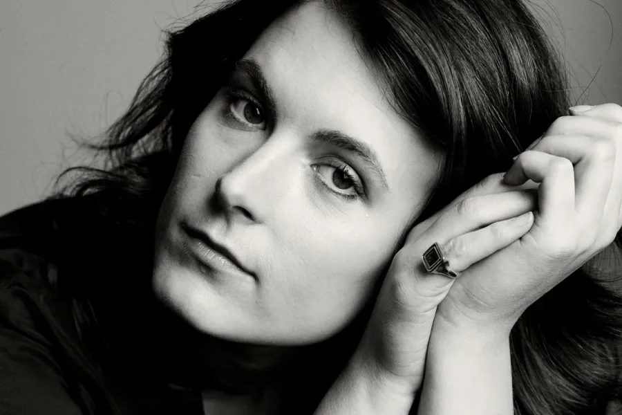 A black and white portrait of a woman from the neck up. Her head is resting on her two hands that are clasped to the side of her face.