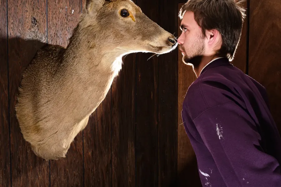 image of person nose-to-nose with taxidermied deer head on wall