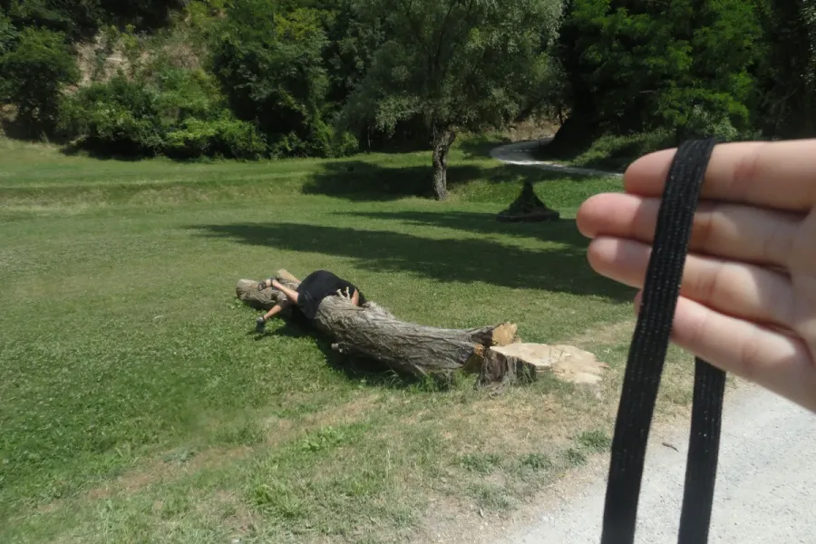 scene with person draped over downed tree trunk with hand in foreground holding black strap