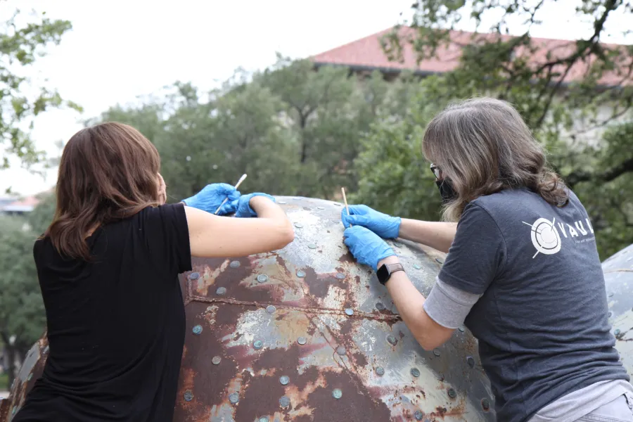 Two volunteers add new pennies to an artwork